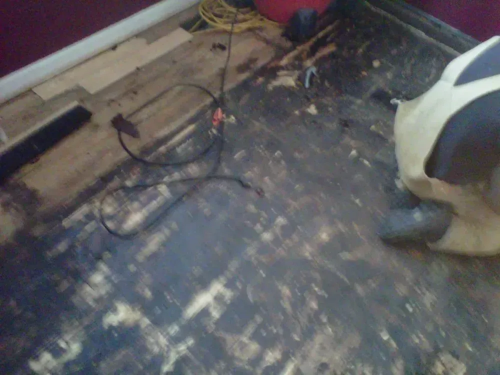 Damaged floor with exposed wires near a wall and a white appliance on the right