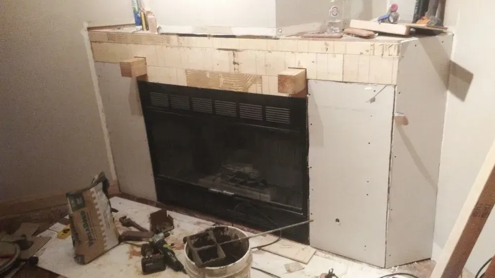 Partially renovated fireplace with exposed framing, white drywall, and tools on the floor