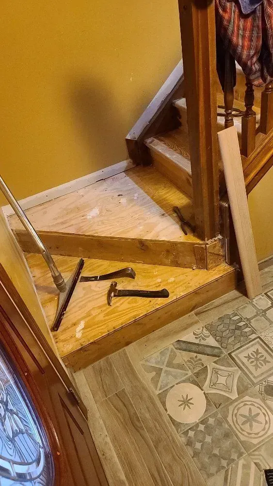 Broken wooden stairs with tools scattered on the floor beside a patterned tile entryway