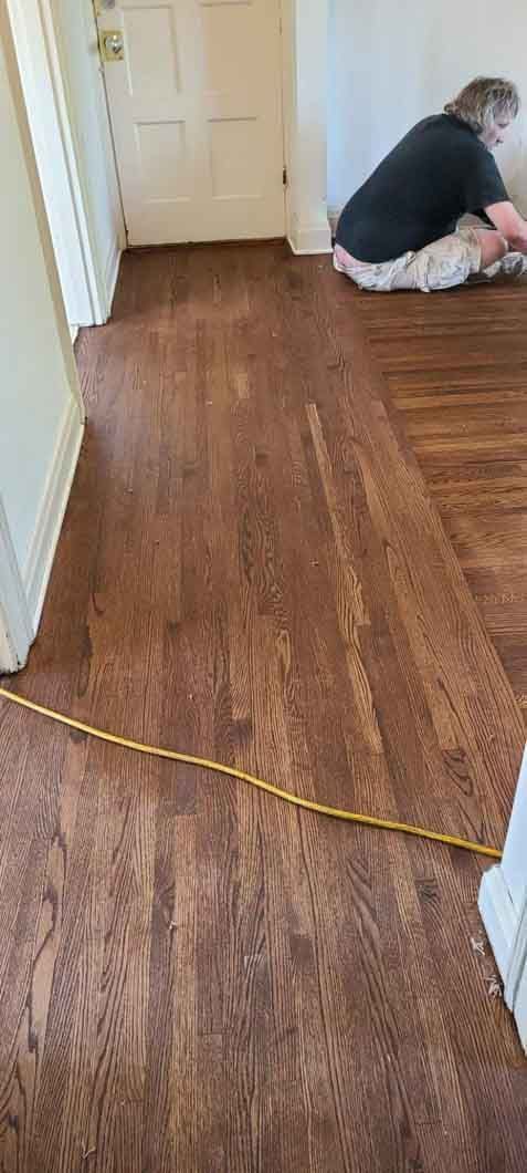 Hallway with a wood floor and a yellow cable, with a person kneeling near a doorway at the far end