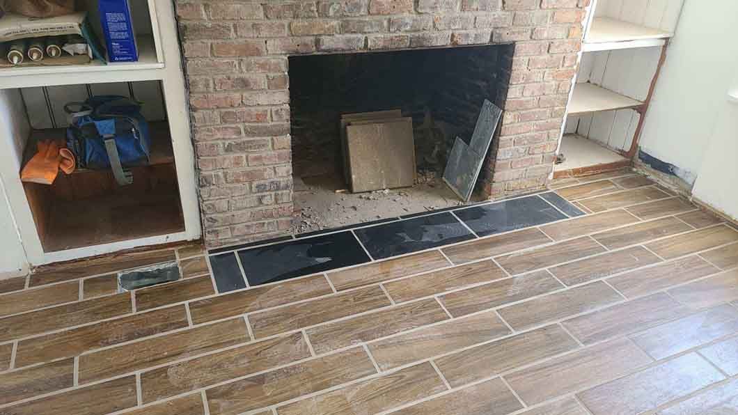 Brick fireplace with a dark opening and tiled hearth in a room with a wooden floor.