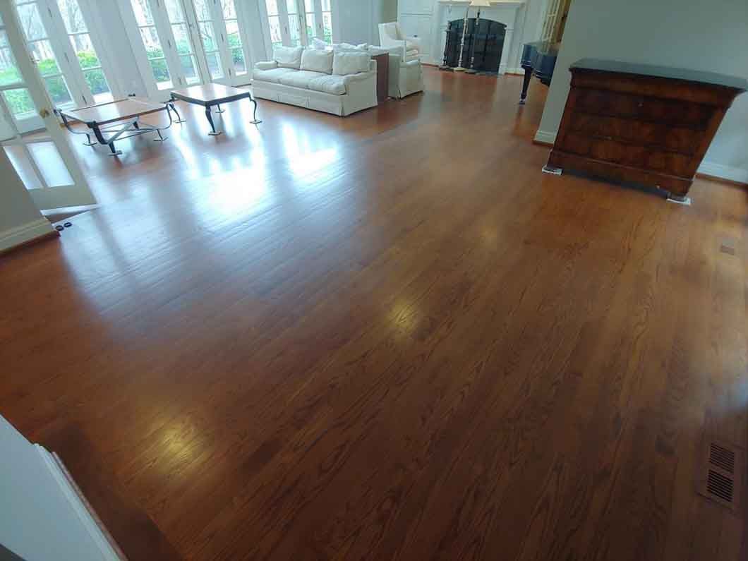 Empty hardwood living room with large windows, white sofa, and brick fireplace.