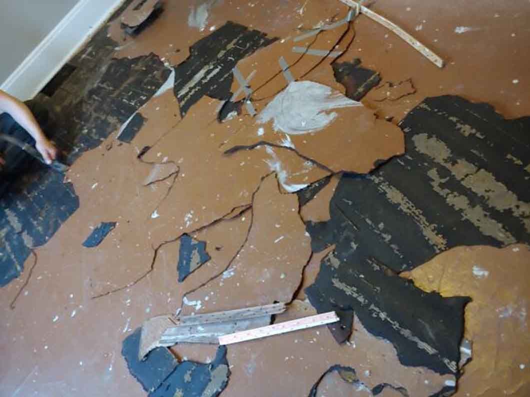 Broken brown floor tiles with exposed dark underlayment and scattered debris