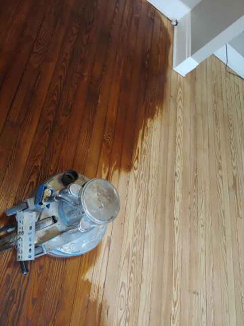 Paint roller and tray on hardwood floor, with a darkly stained section nearby