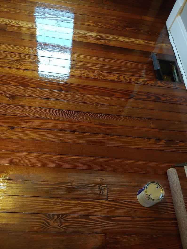 Glossy wooden floorboards with sunlight reflection, a paint can, and a small patch being repaired