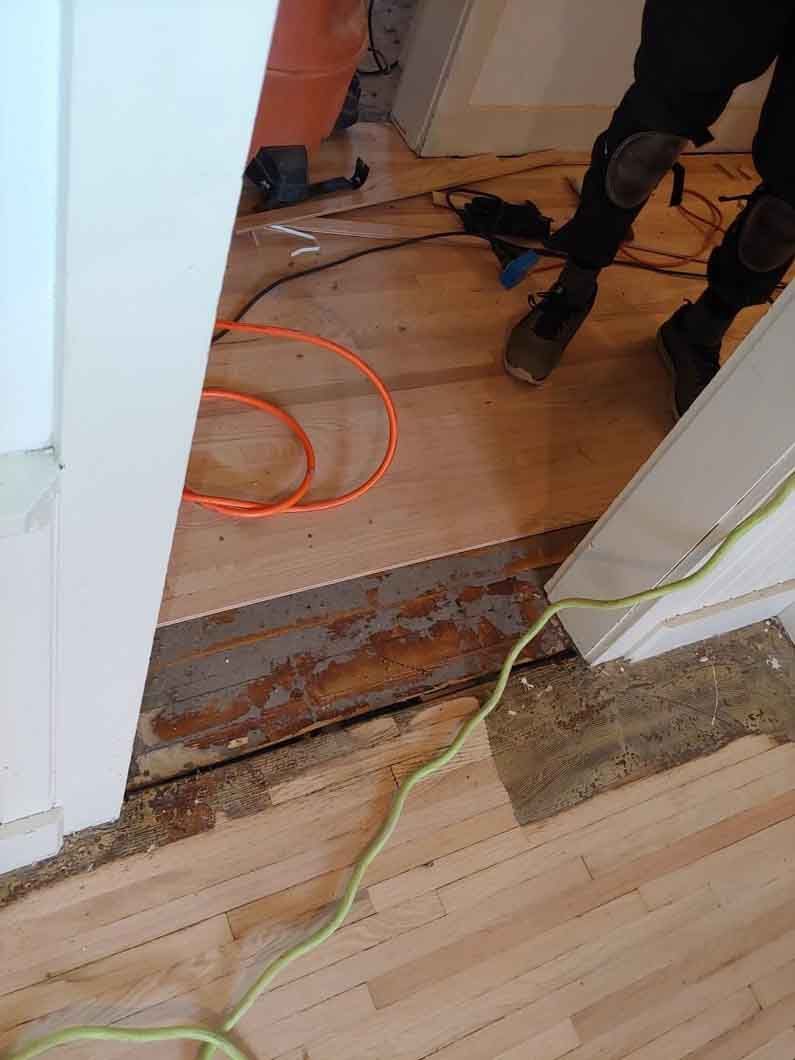 Home doorway with exposed floor edges, cables, and a worker’s legs in the background