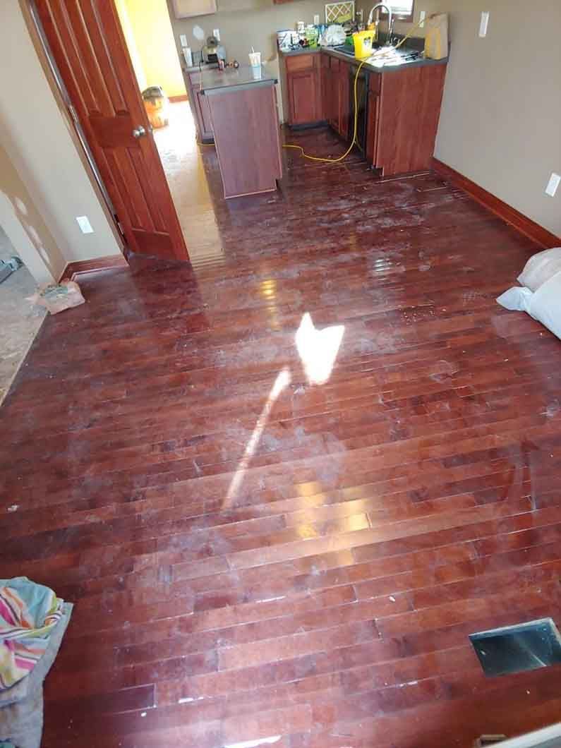 Wooden-floored room with a small kitchen area and bright sunlight reflecting on the floor.