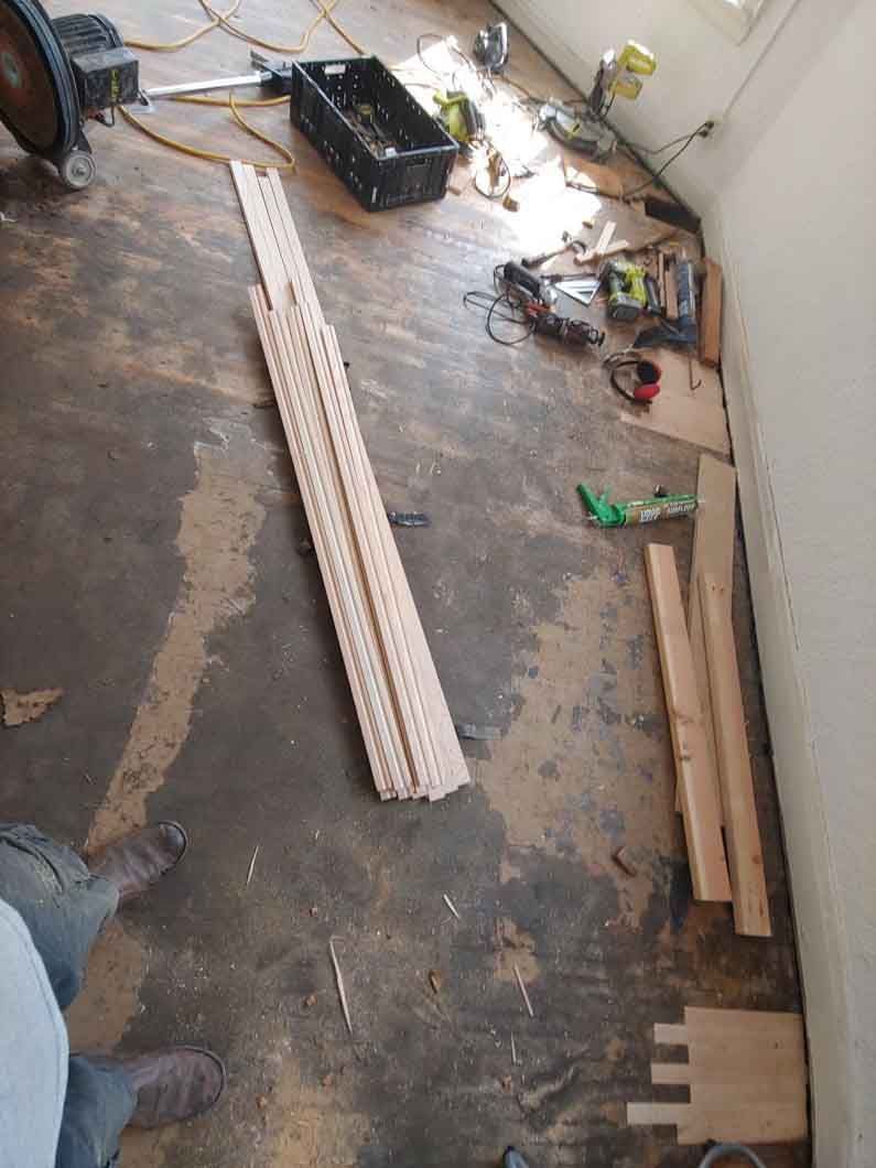 Construction area with long white panels, wooden planks, and tools scattered on a dusty floor.