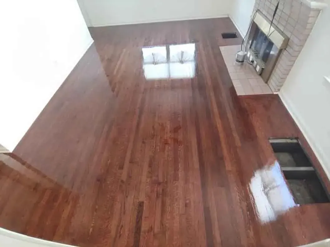 Empty room with glossy wood floor, white walls, and two small floor vents near a fireplace.