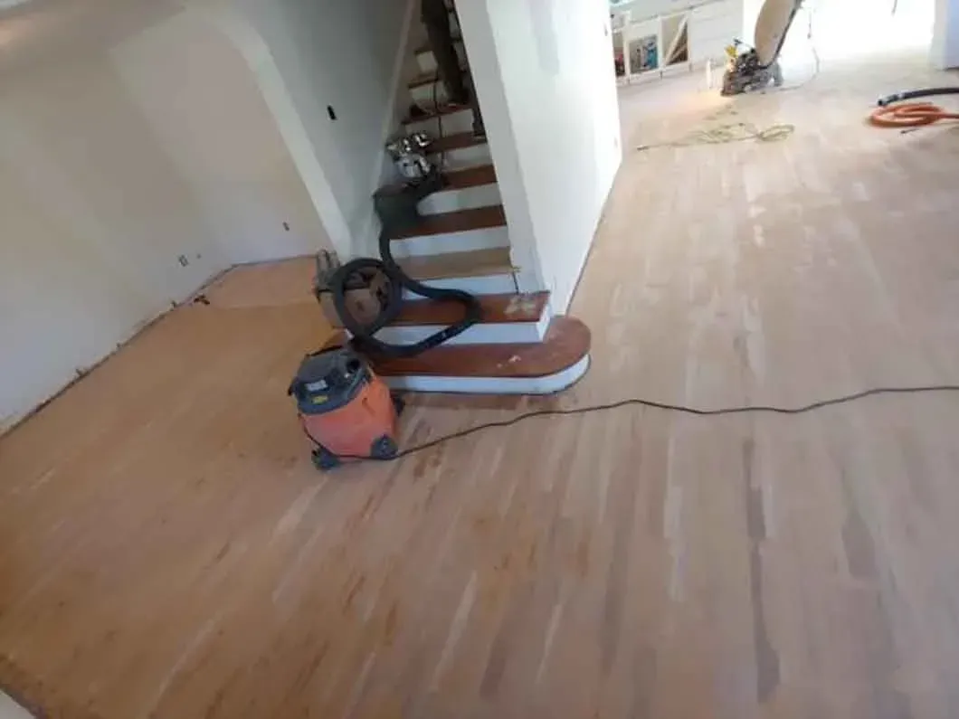 Dusty hardwood floor and staircase in an unfinished room, with a vacuum and hoses in the foreground.