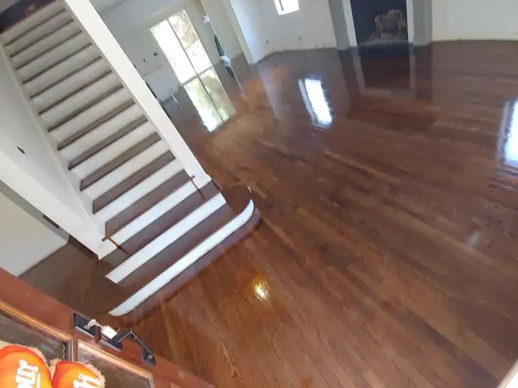 Empty room with glossy hardwood floors, staircase on the left, and bright windows.