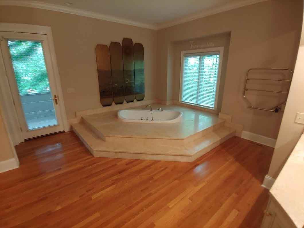 Bright bathroom with a large corner soaking tub, hardwood floor, and windows on two sides.