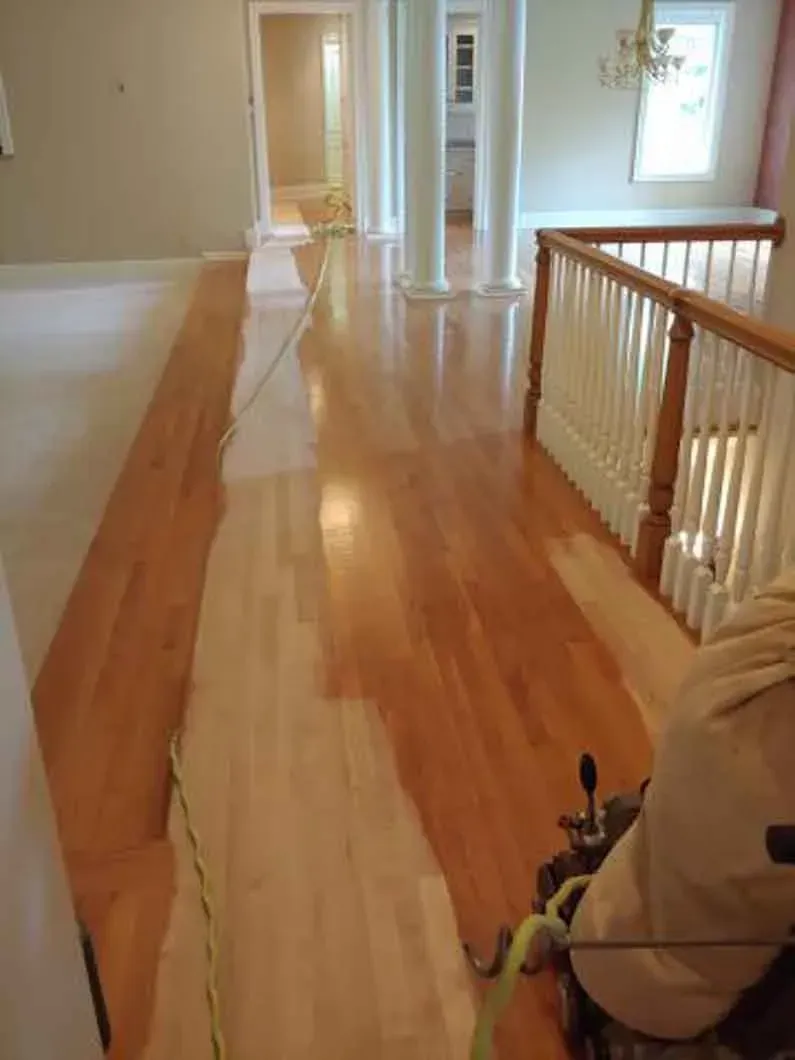 Wooden hallway with polished floor, white railing, and a chair at the right edge.