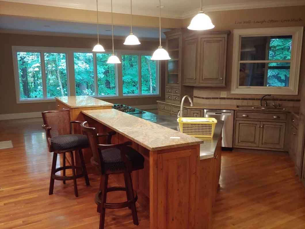 Spacious kitchen with wood floors, long island, pendant lights, and large windows overlooking trees