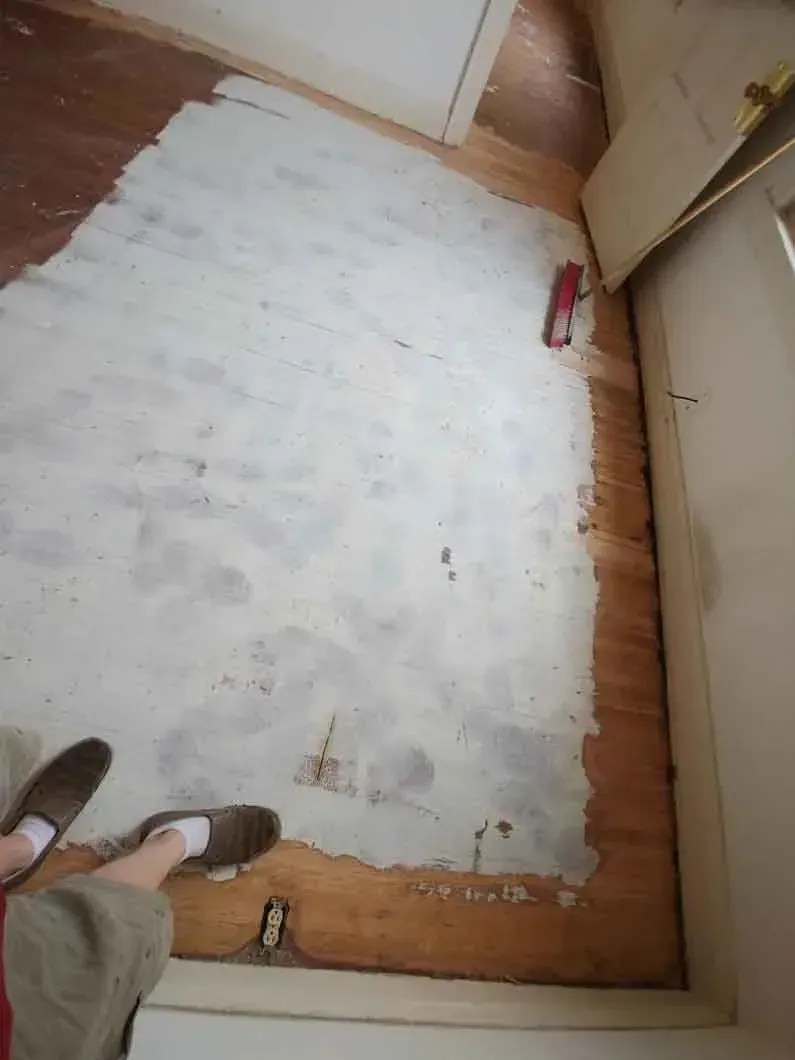 Large white rug on a wooden floor in a small room, with a person’s feet visible at the bottom left.