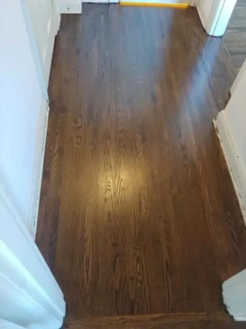 Narrow hallway with dark wood flooring and white walls, lit by warm ceiling light.