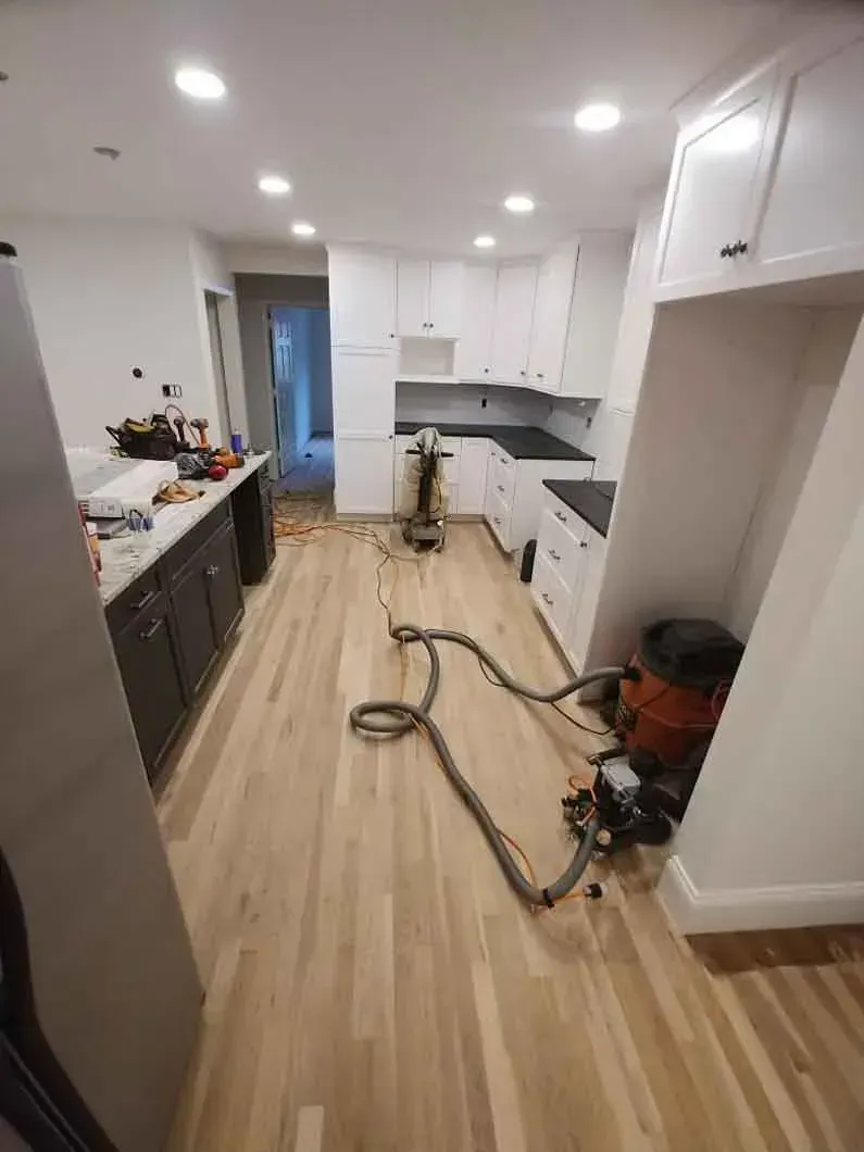 Renovated kitchen with white cabinets and wood floor, tools and vacuum hose on the floor during cleaning or work