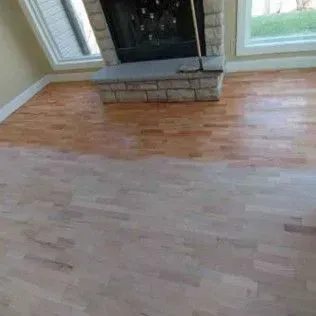 Wooden floor in a living room with a stone fireplace and large windows.