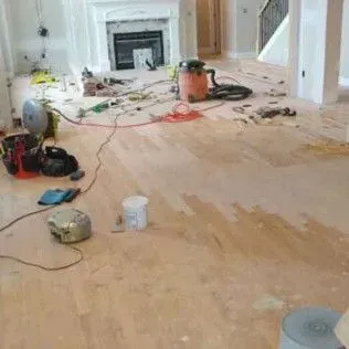 Renovation room with tools and debris scattered across a partially sanded wooden floor.