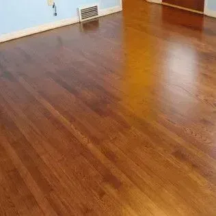Empty room with glossy brown hardwood floor and a small wall vent