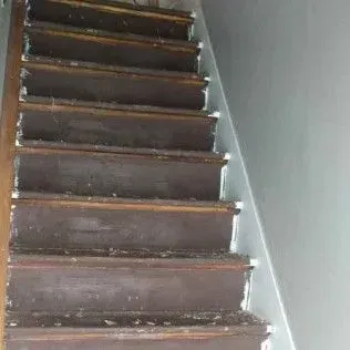 Narrow wooden staircase with worn dark steps and white walls, viewed from below