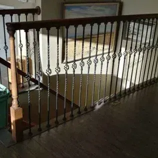 Wooden stair railing with black metal balusters in a dim indoor hallway.