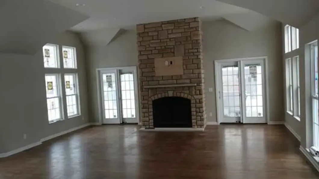 Empty living room with dark wood floors, stone fireplace, and multiple French doors and windows.