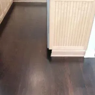 Dark wood floor with a white radiator and baseboard in a hallway corner