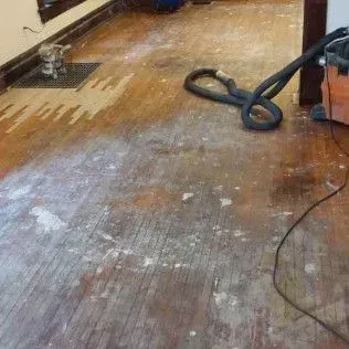 Dusty wooden floor being sanded, with a vacuum hose on the right.