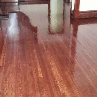 Shiny wooden floor in an empty room with table legs and a cabinet in the background