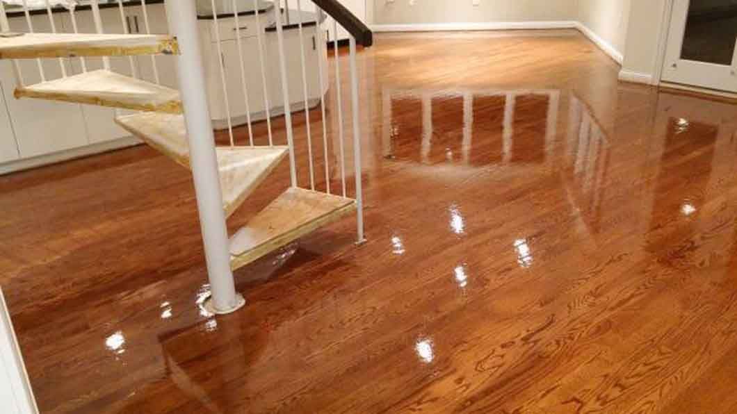 Polished hardwood floor with staircase railing and bright room reflection
