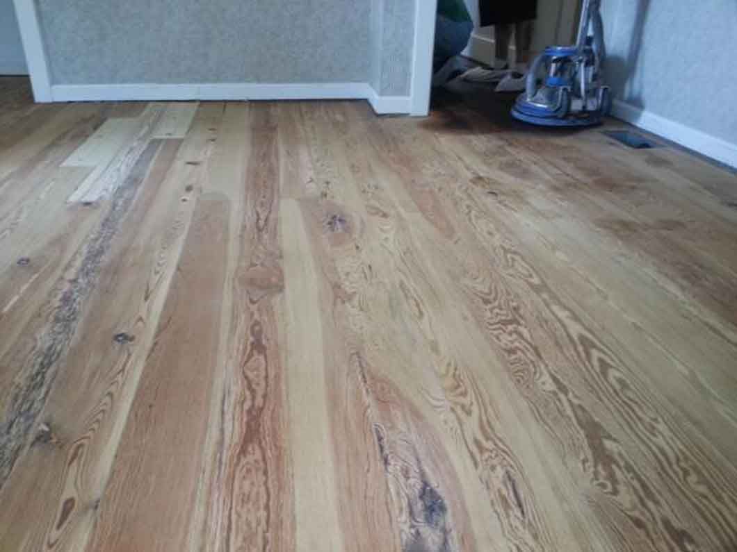 Empty room with light wood flooring and a vacuum cleaner in the back corner.