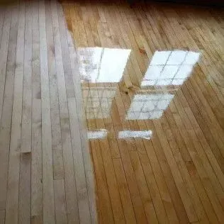 Wooden floor reflecting a bright window with grid panes.