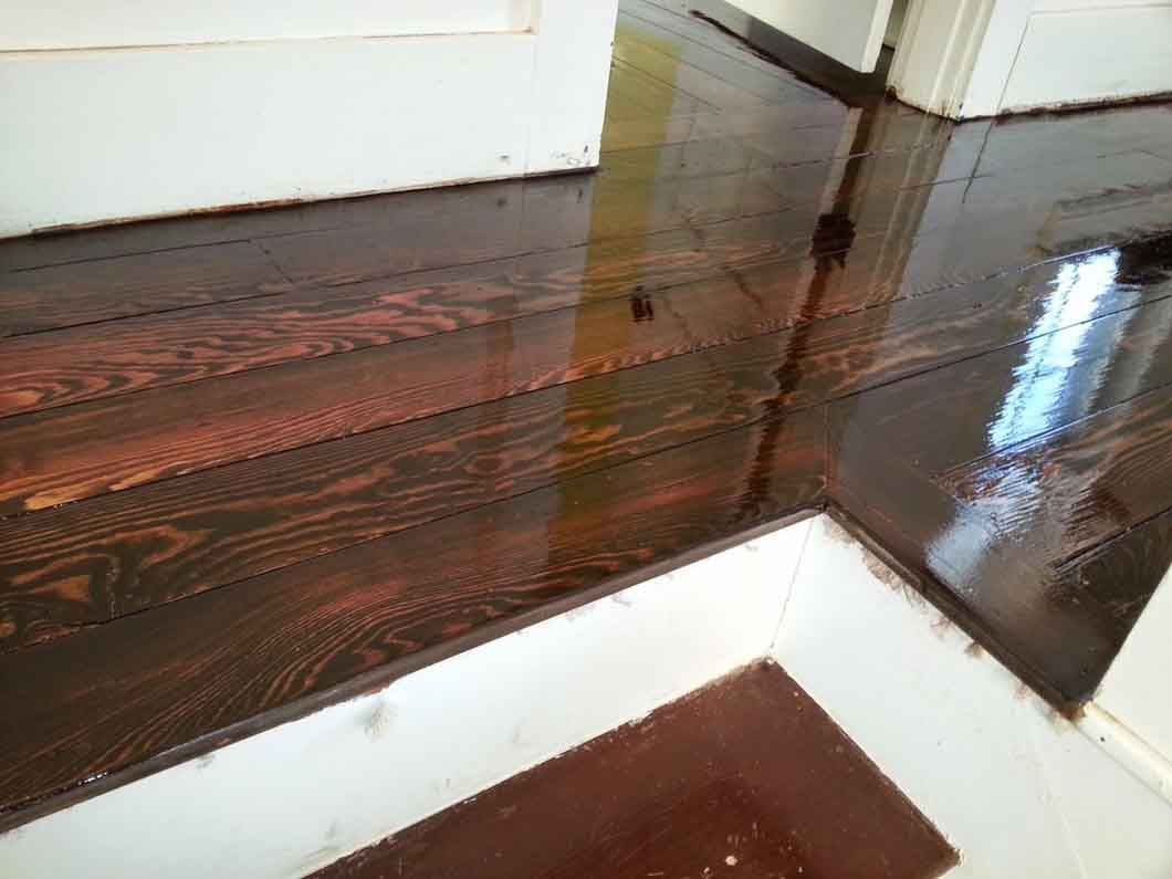 Wooden stair landing with a glossy dark finish and white walls, reflecting light.
