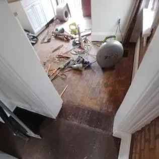 Messy hallway with scattered tools, cables, and debris on a wood floor during home repair