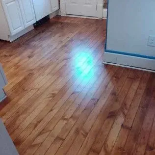Empty kitchen corner with wood flooring and white cabinets, showing a bright light reflection on the floor