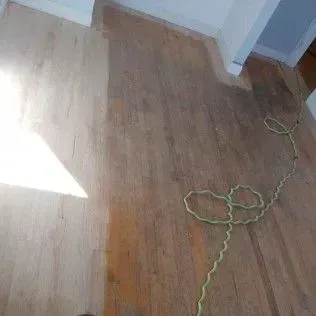 Empty room with hardwood floor, bright sunlight, and a green rope or cord on the floor.