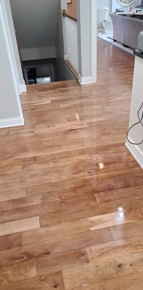 Wooden hallway floor with a stair opening and kitchen appliances in the background