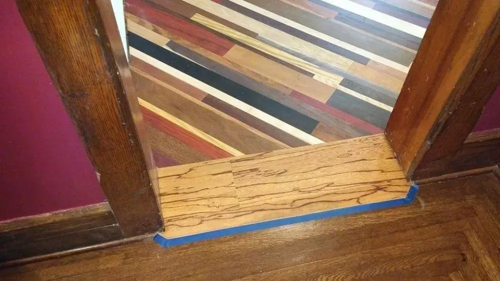 Doorway with a wooden threshold taped over, leading to a striped rug and hardwood floor.