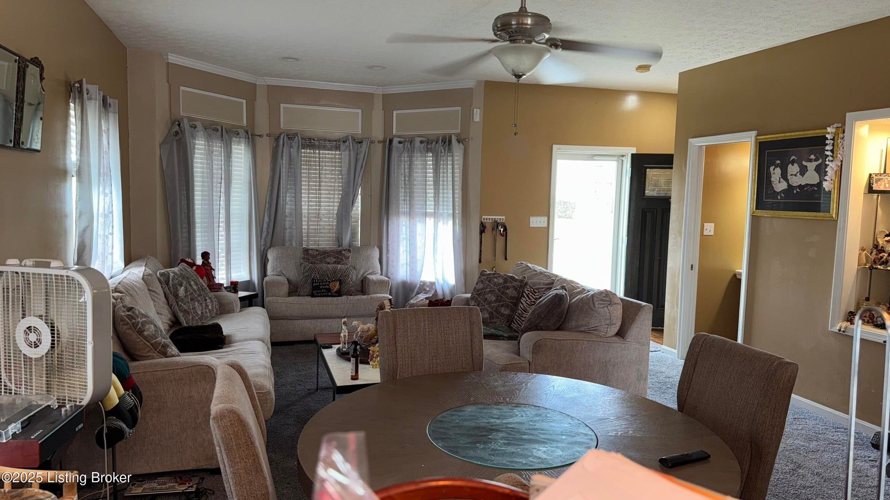 Cozy living room with sofas, round dining table, ceiling fan, and bright windows with curtains