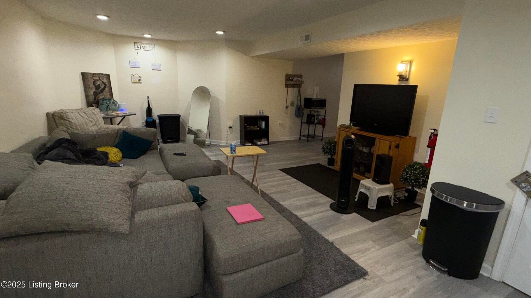 Cozy living room with gray sectional, TV, fireplace, lamp, and a pink notebook on the sofa.