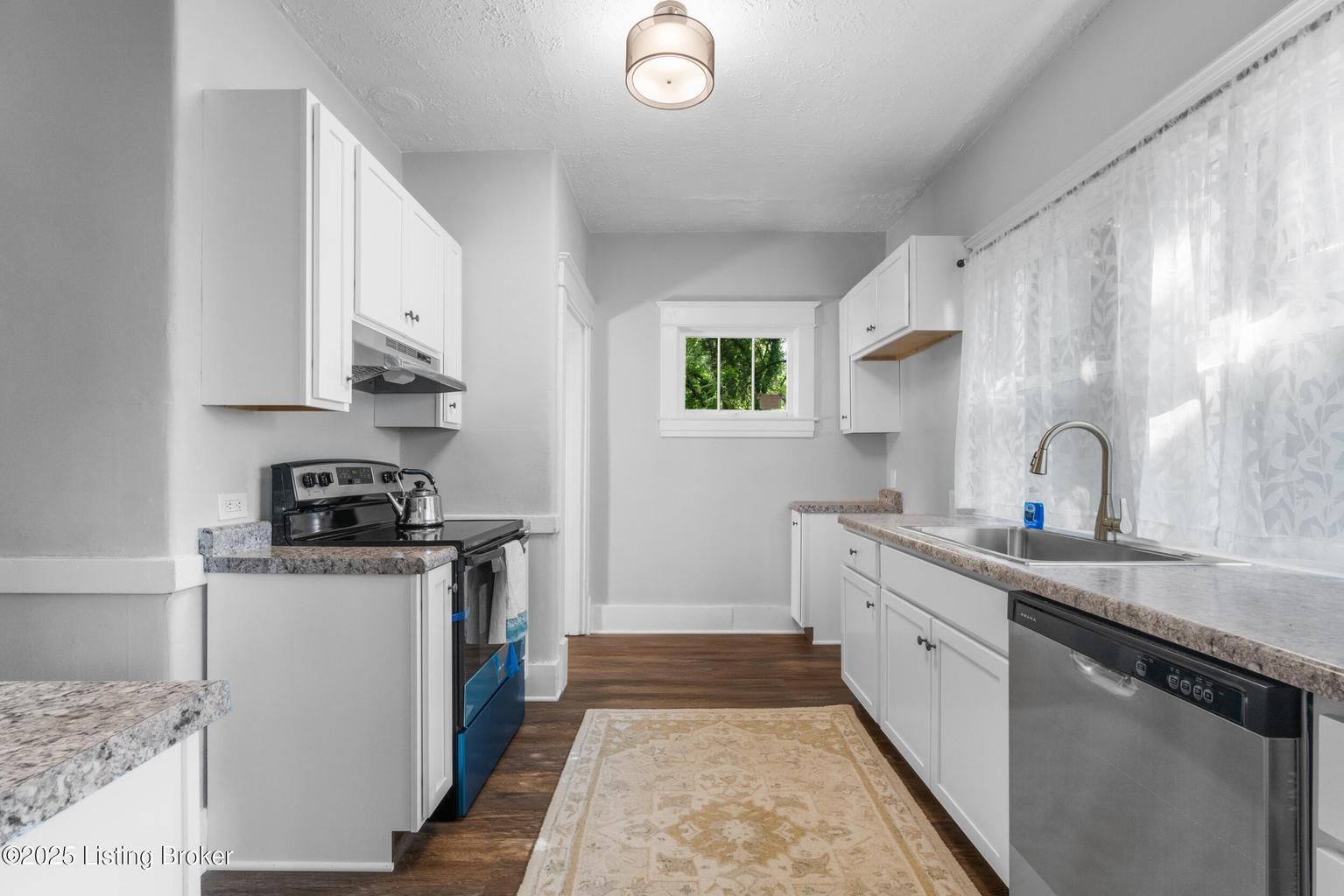 Bright white galley kitchen with granite counters, blue oven, and a window at the end.