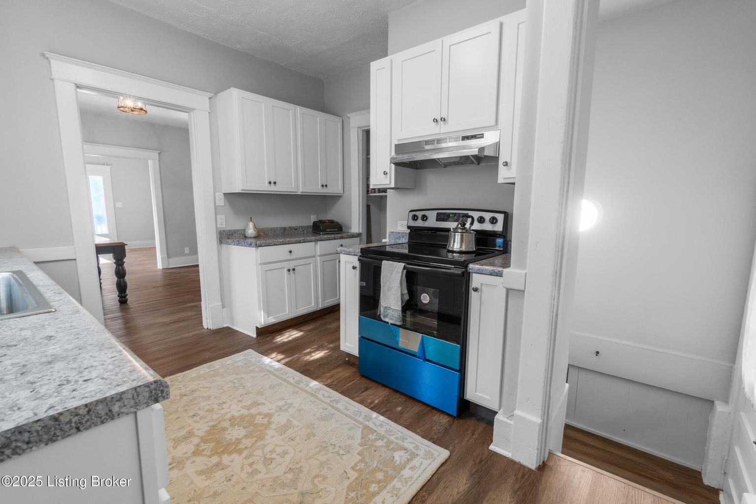 Small kitchen with white cabinets, black stove, and blue oven cover beside a gray countertop and rug.