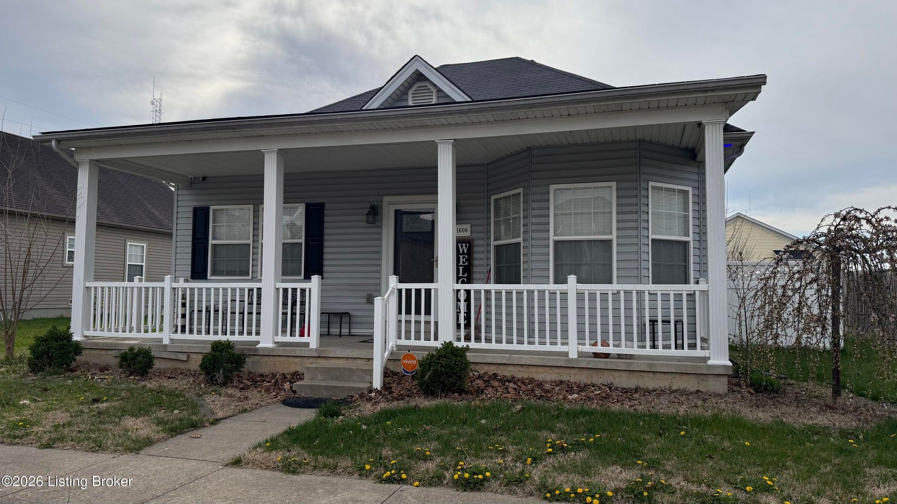 Small gray house with a white porch, columns, and black roof under a cloudy sky