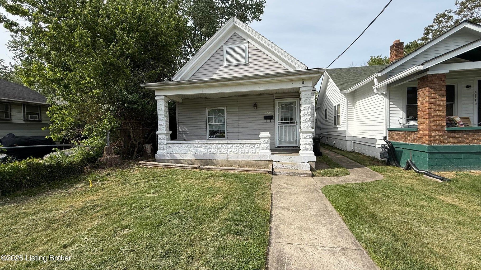 Small white house with a front lawn and concrete walkway on a sunny day