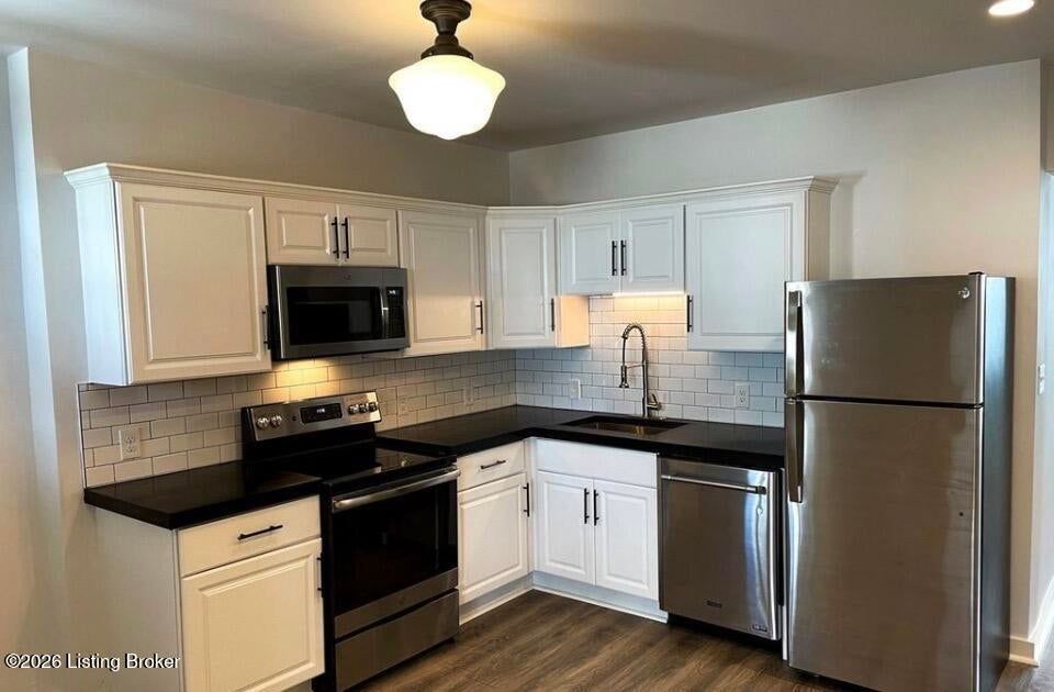 Modern white kitchen with black countertops, stainless steel appliances, and wood flooring