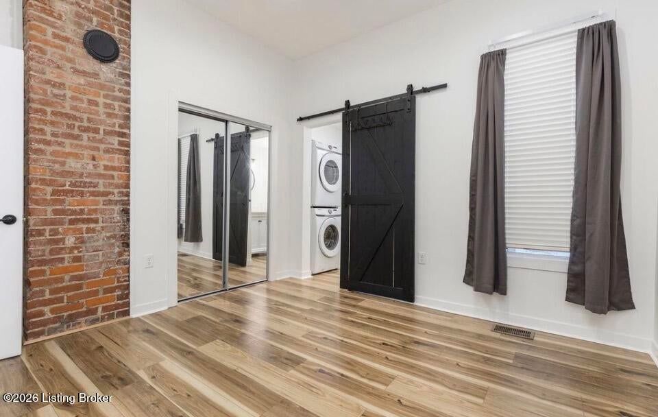 Empty room with hardwood floors, brick accent wall, mirrors, and black sliding barn door.