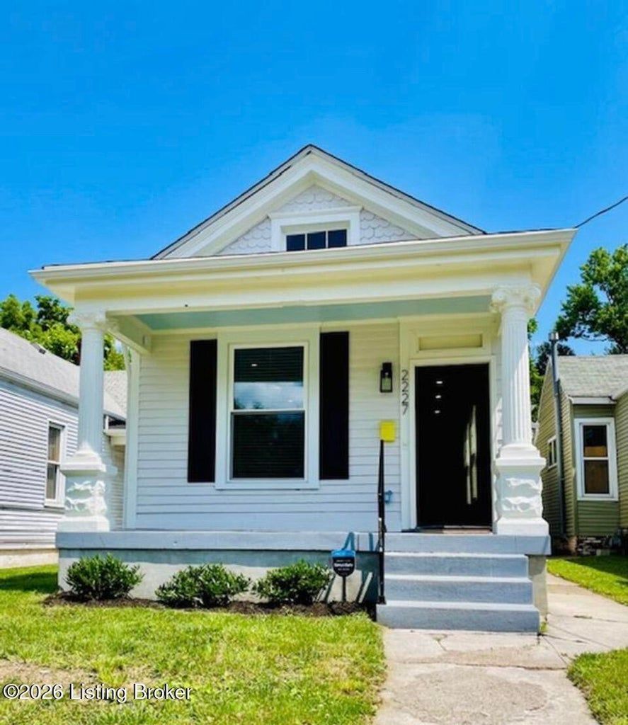 Small white house with front porch, black shutters, steps, and a blue sky overhead