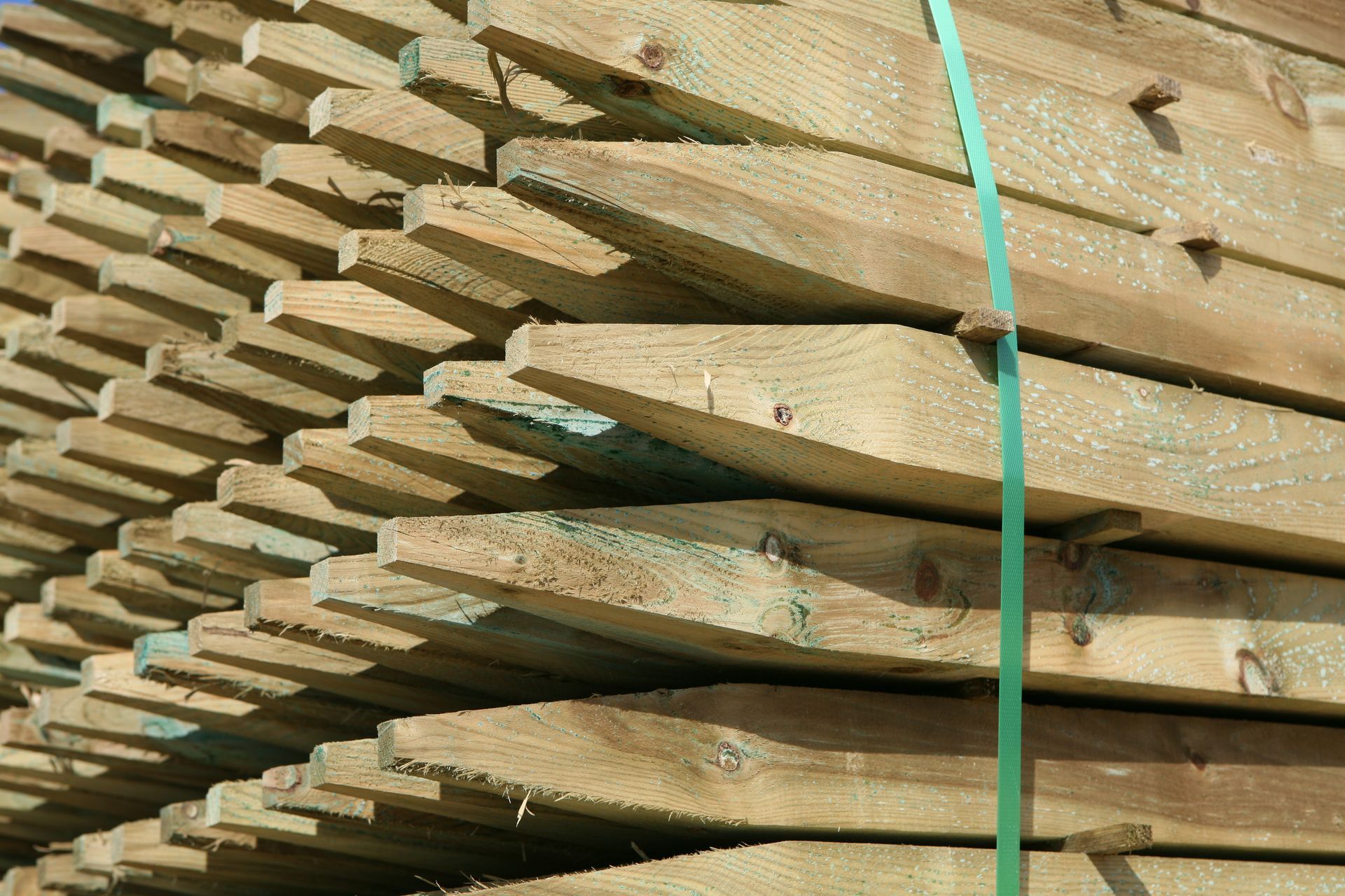 Stacked wooden boards with a green strap binding them together outdoors.