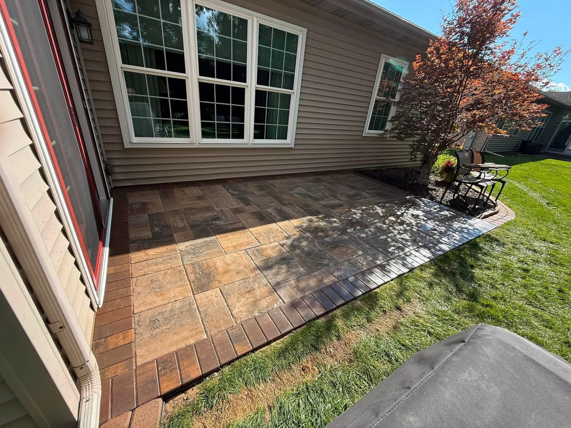 Brick patio beside house with a worker installing pavers near a flower bed